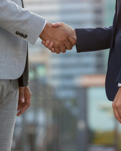 Businesspeople standing in city street and shaking hands. Business man and woman in office suits meeting outside. Successful partnership concept